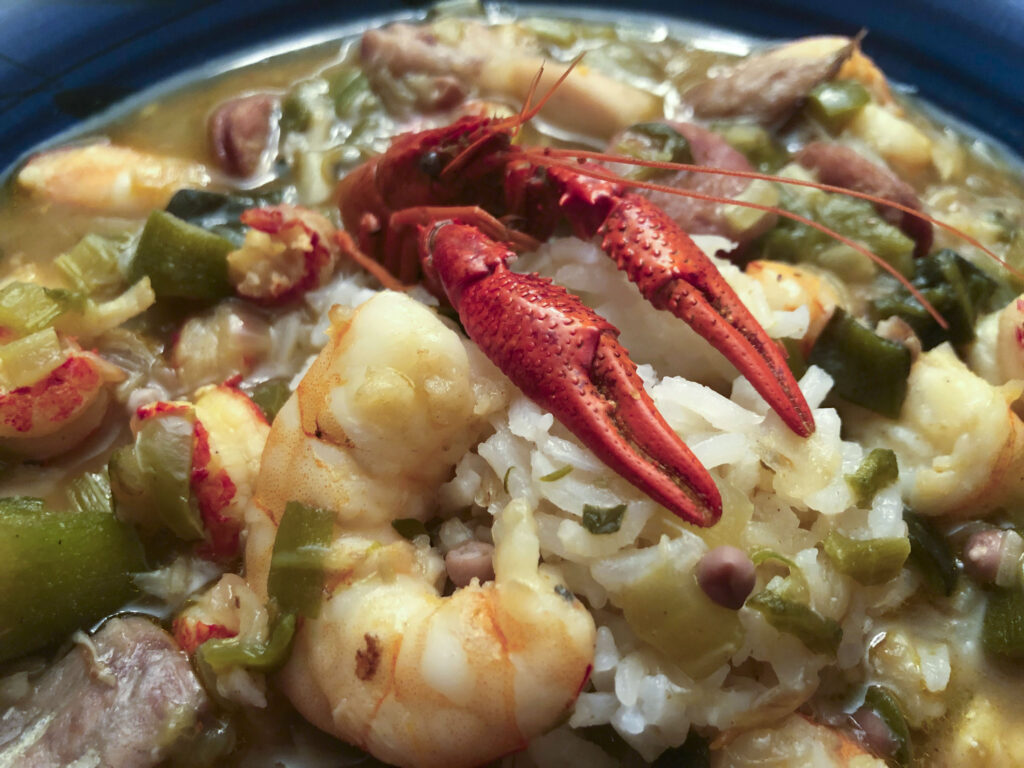 A hearty seafood rice stew topped with red crawfish and plump shrimp, mixed with sausage and green vegetables; its rustic, comforting meal feels inviting.