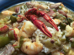 A hearty seafood rice stew topped with red crawfish and plump shrimp, mixed with sausage and green vegetables; its rustic, comforting meal feels inviting.