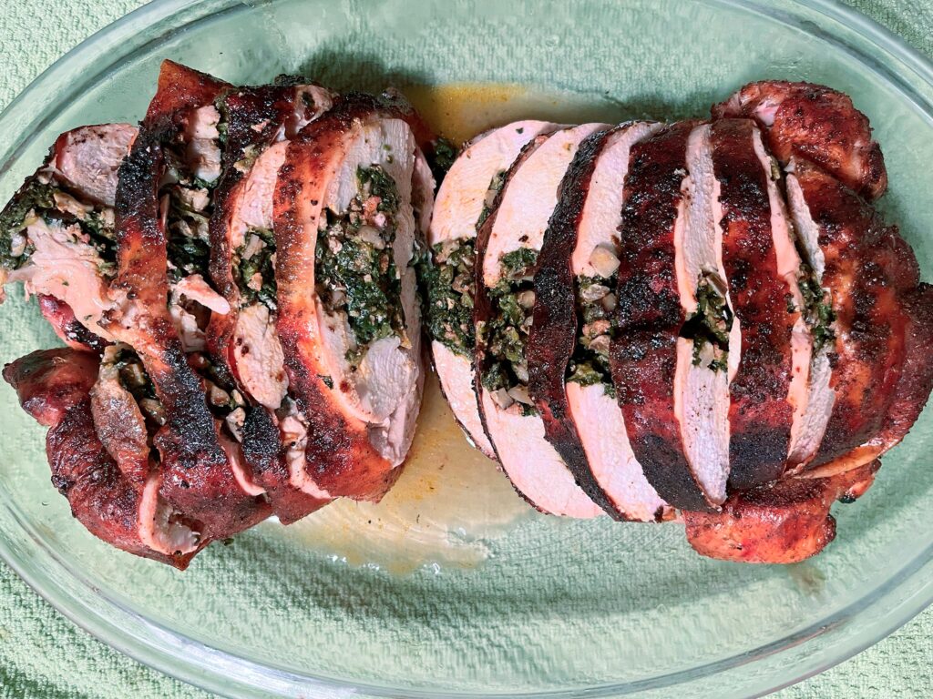 Sliced stuffed whole chicken with a browned, charred crust rests on a glass platter, showing a juicy pink interior and a hearty, inviting meal.